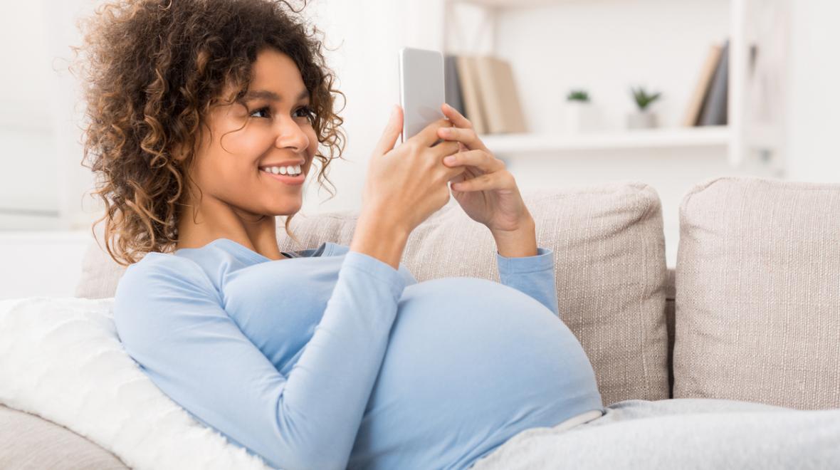 pregnant woman on the couch looking at her cell phone smiling