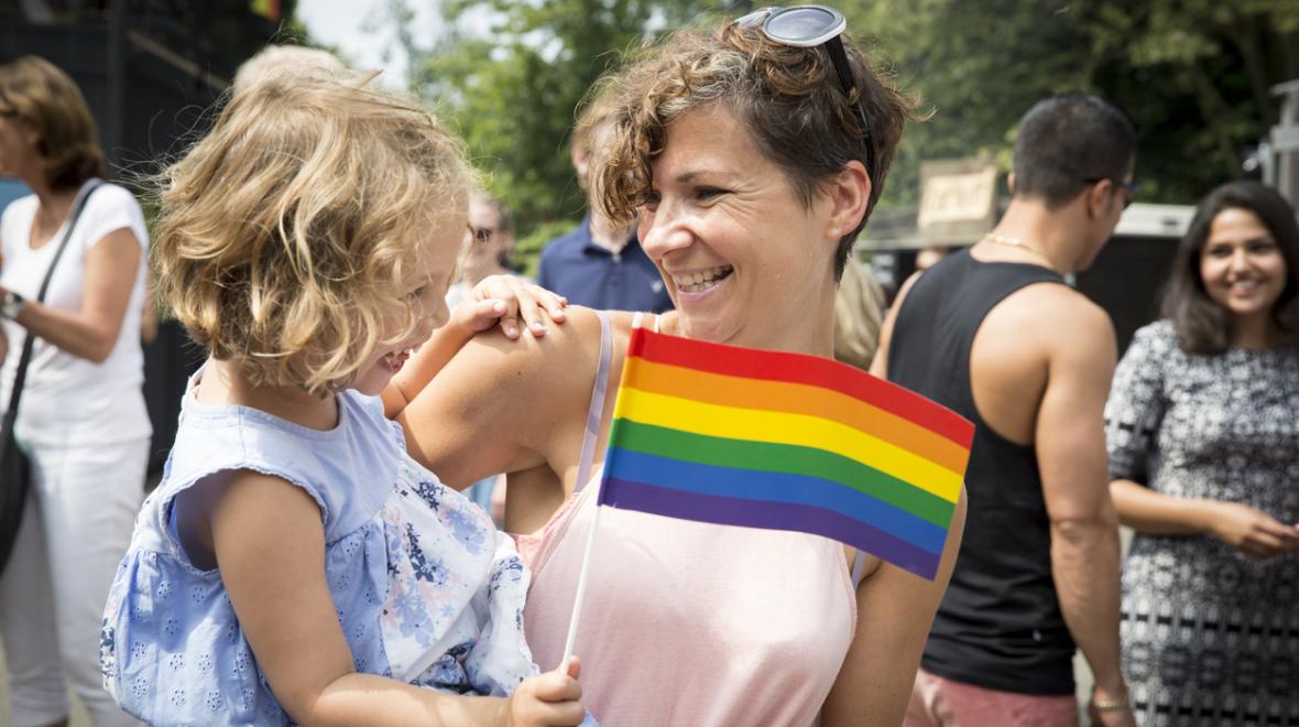 mother hugging her daughter at a pride parade with daughter holding the pride flag