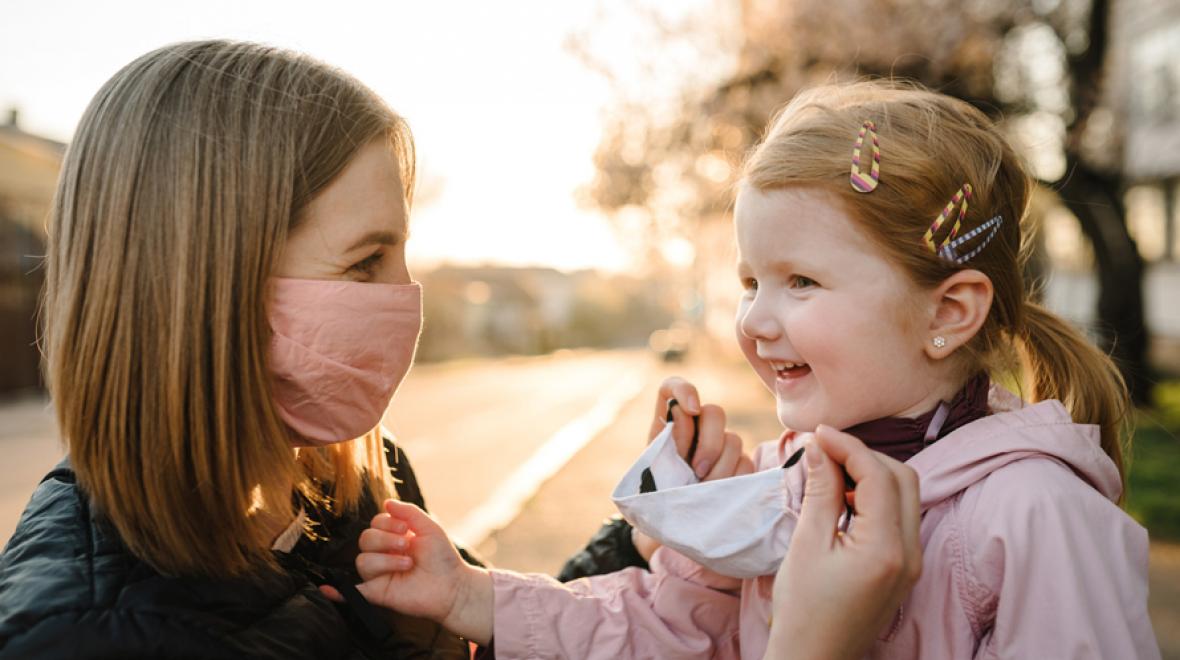 mom putting a mask on her smiling daughter