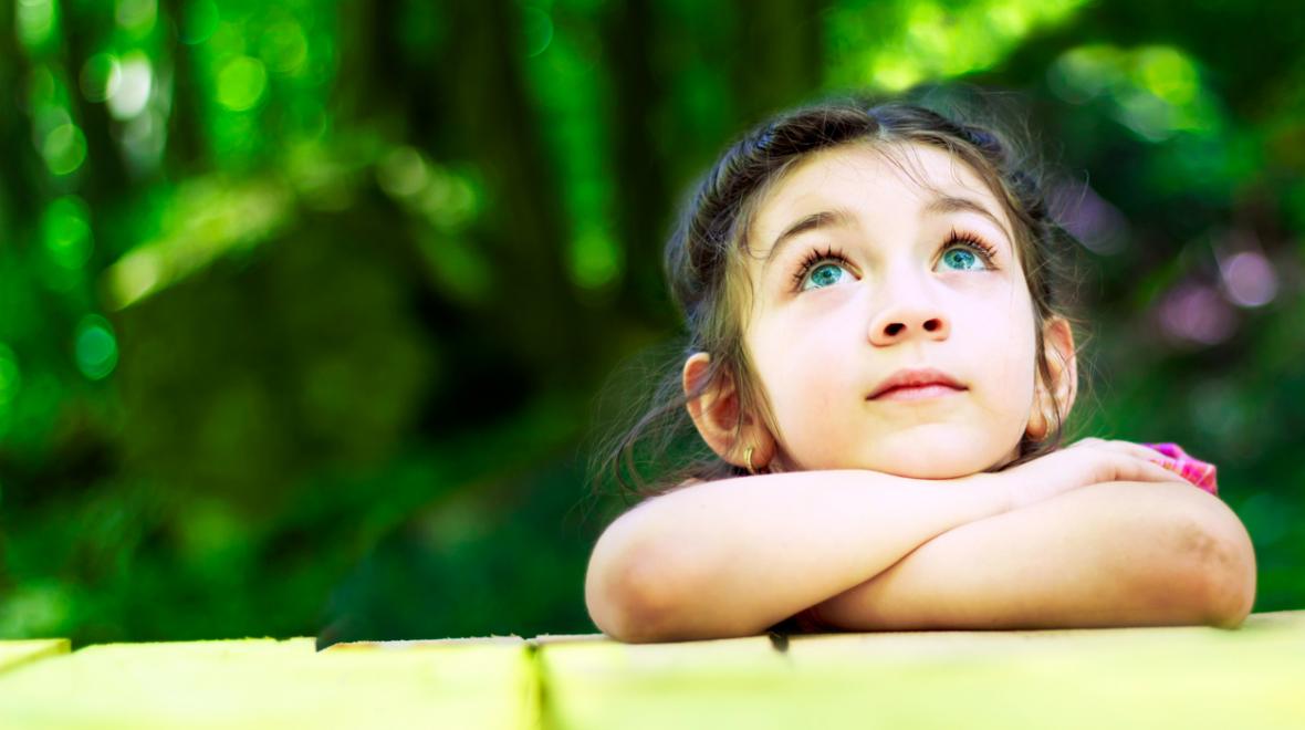 little girl outdoors leaning her crossed arms on a table looking up at the sky