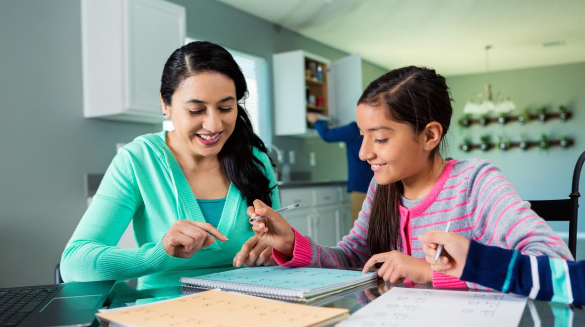 Mother helps her tween daughter with her homework at the kitchen table
