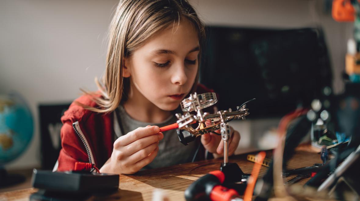 girl learning robotics in her room at home with robot parts on her desk