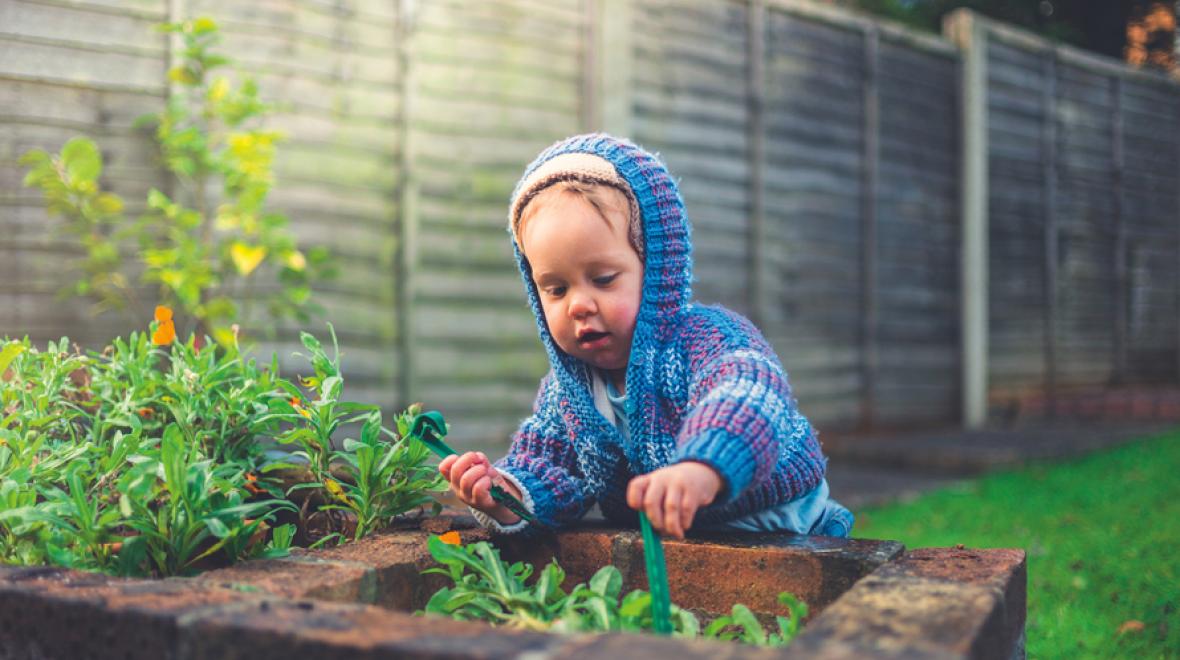 little boy leaning over a raised garden bed wearing a hooded sweater