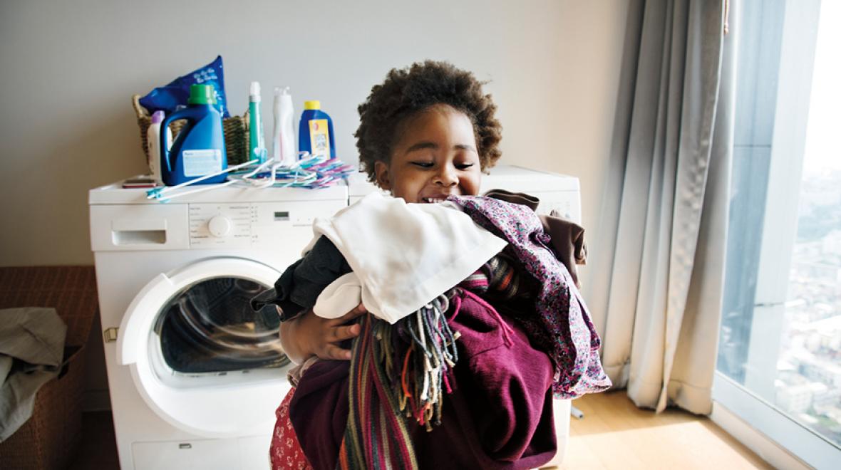 girl with an armful of laundry with the washer dryer in the background