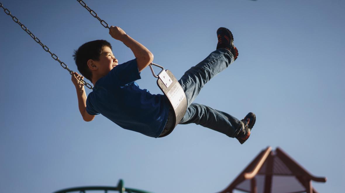kid on a swing soaring high with blue sky in the background