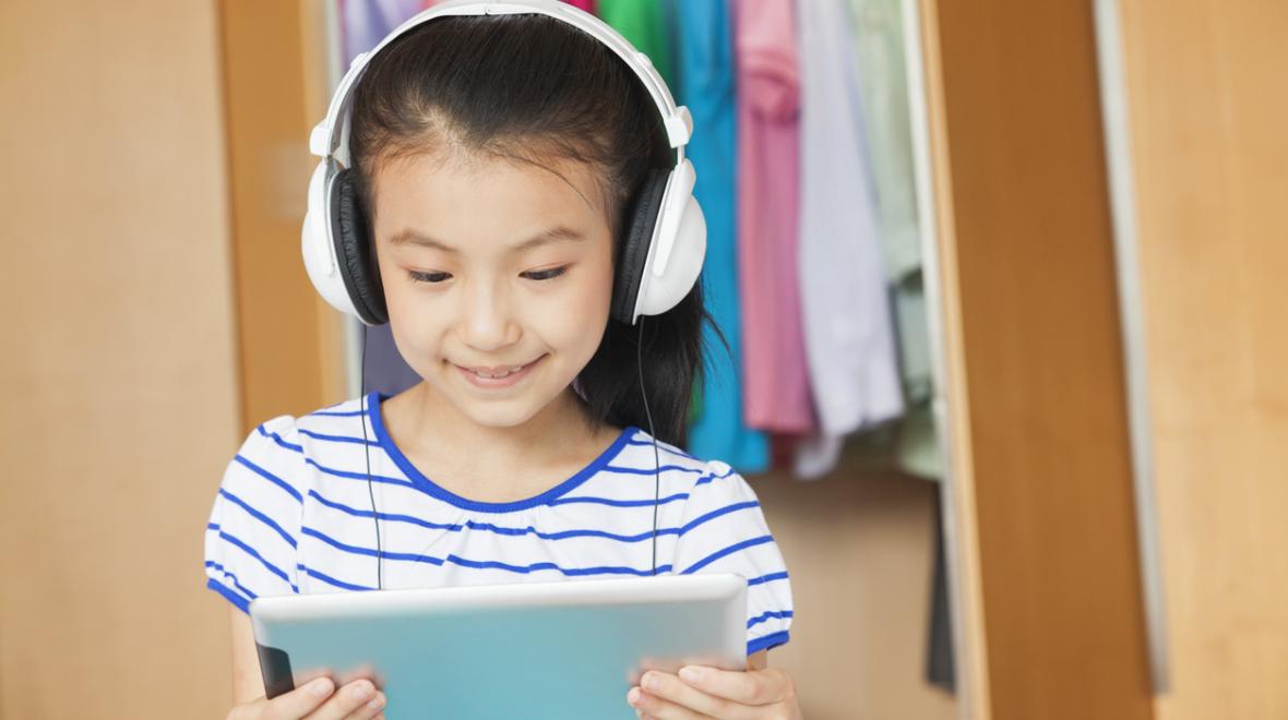 Young girl wearing headphones and viewing content on a tablet computer