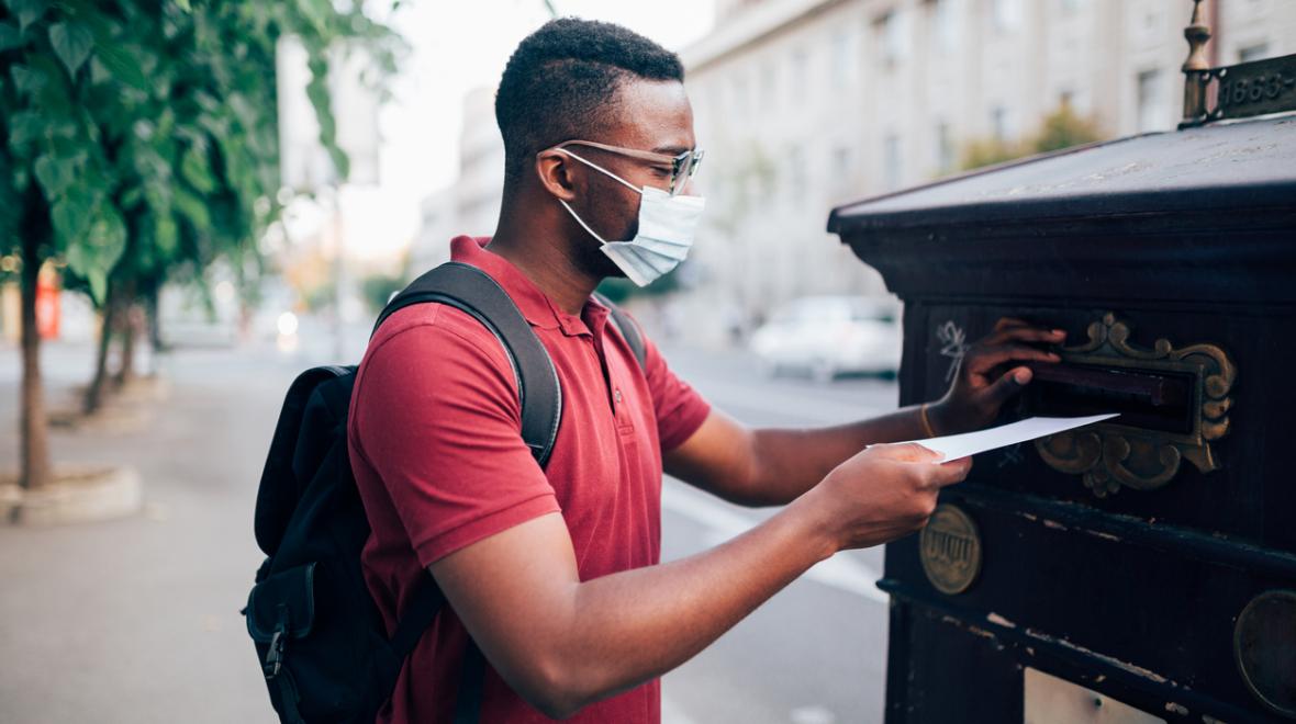 black teen wearing a mask putting his ballot in the mail