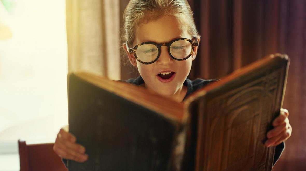 Young boy wearing glasses reads a magical book