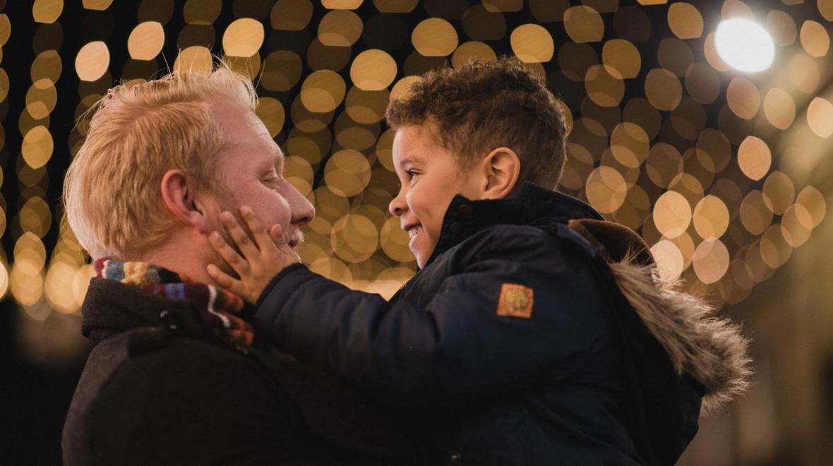 Dad and son looking at each other happily with holiday lights in the background