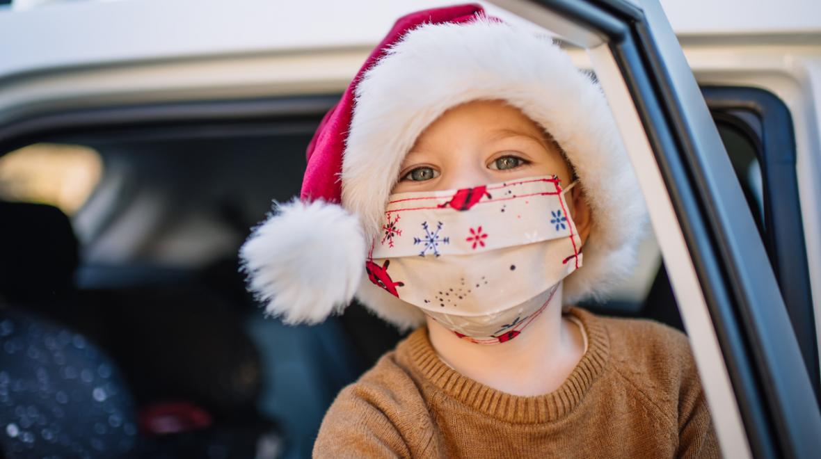 Little boy wearing protective face mask and Santa hat in car on Christmas