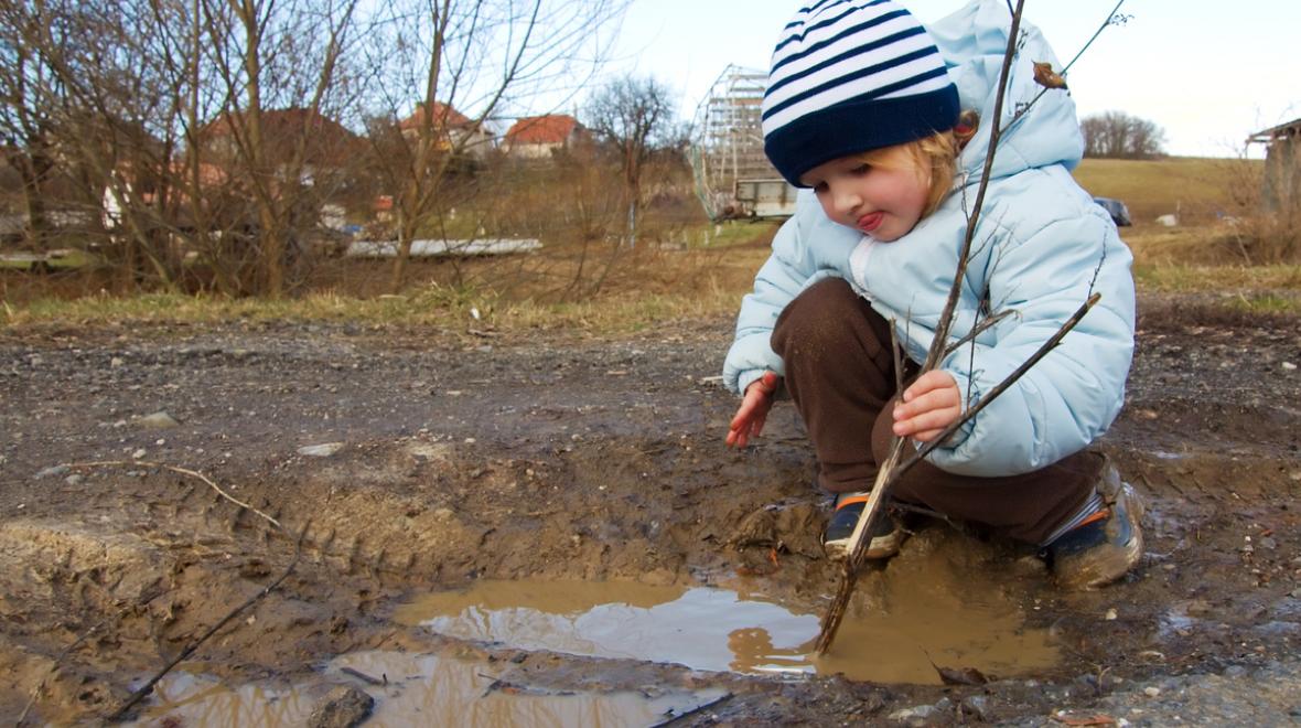 Girl playing with a stick in a mud puddle