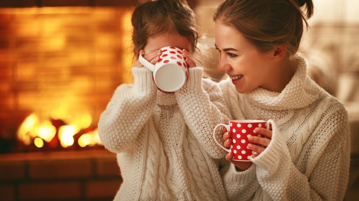 mother and daughter drinking hot cocoa in front of a fire