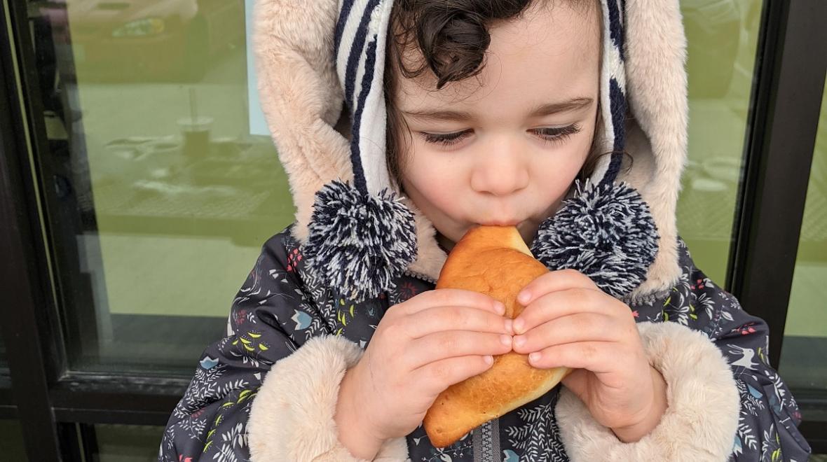Young girl in warm jacket taking a bit of an East African coconut doughnut called mahamri Spice Bridge Food Hall Seattle Tukwila