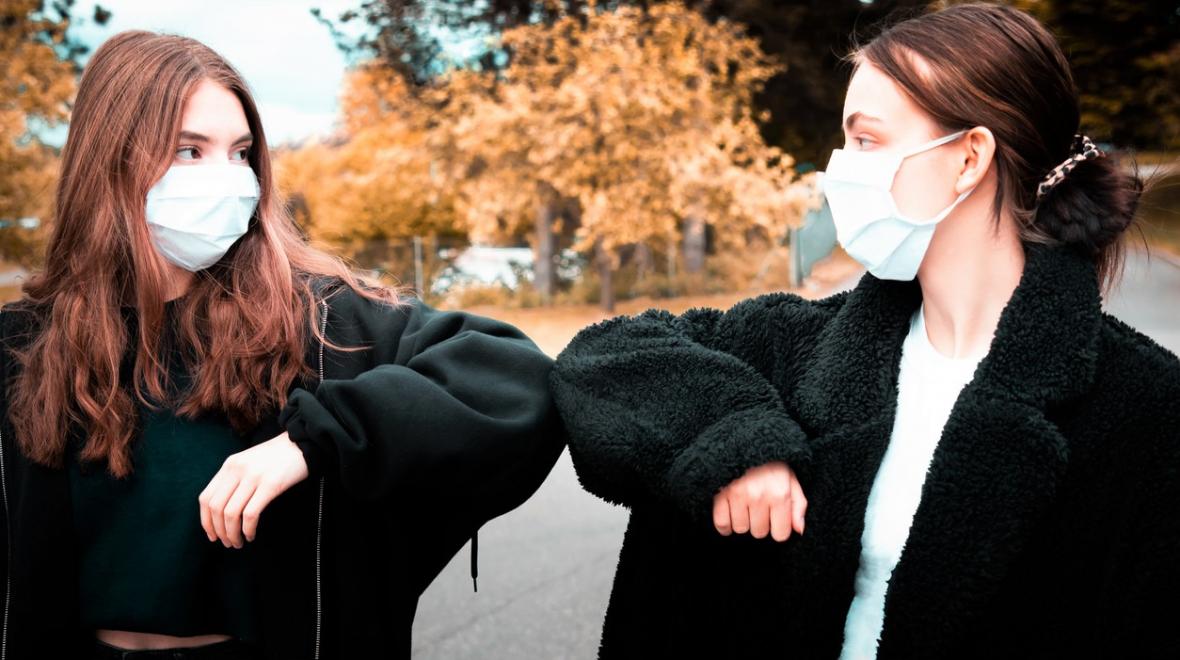 Teen girls wearing masks and black jackets elbow-bumping in an outdoors location mid-winter break camps Seattle Tacoma Bellevue