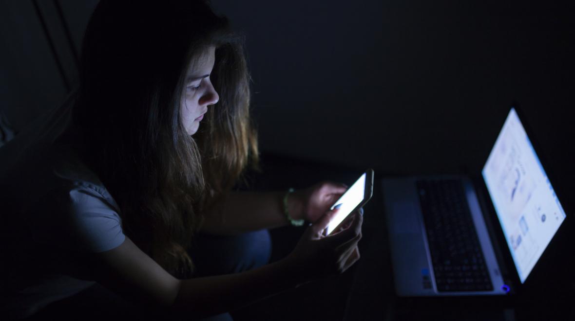 teenage girl in the dark with her laptop and phone screens lit up
