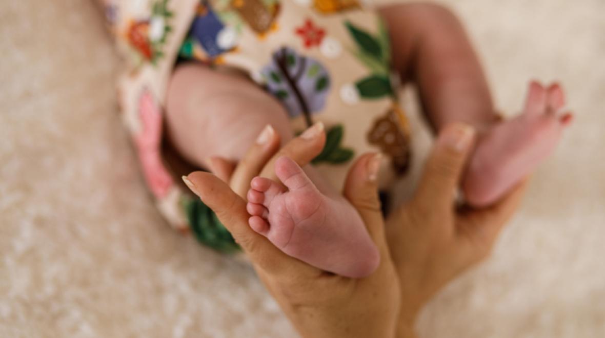 closeup of a baby's cloth diaper with cartoon leaves and a mother's hand holding onto the baby's leg