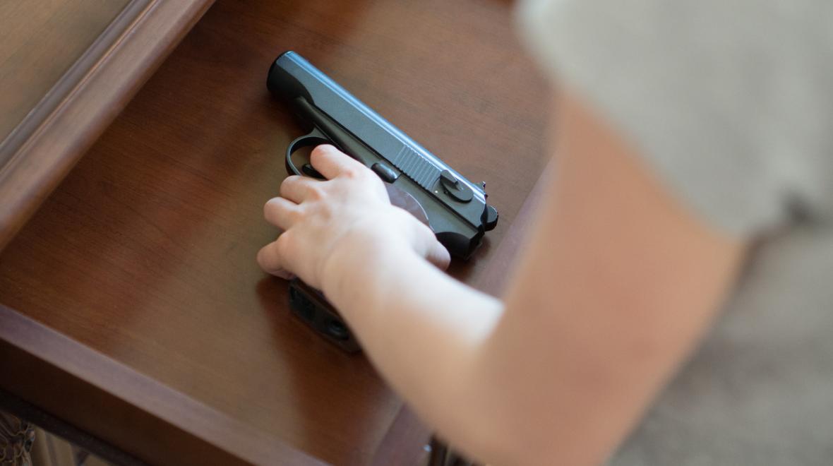 child's hand on a gun inside a drawer