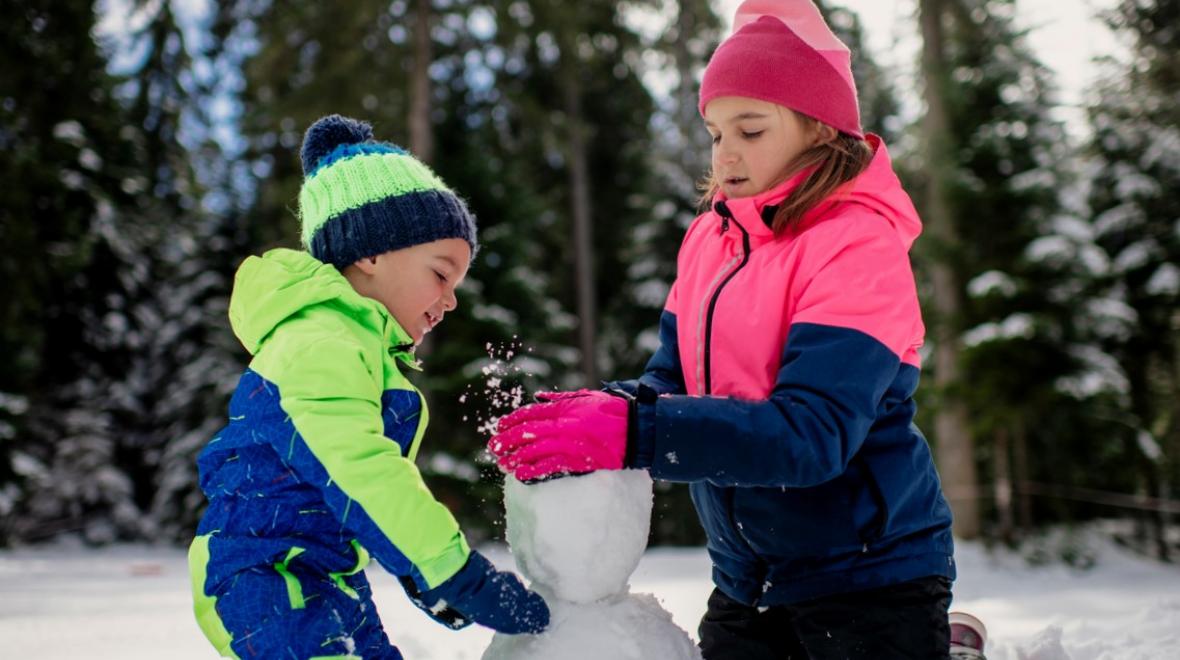 Brother and sister about ages 6 and 8 wearing snowsuits together build a snowman at new Seattle-area Sno-Park at Lake Easton along Interstate 90