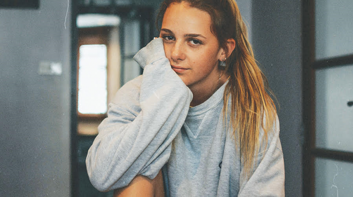 Teenage girl in a sweatshirt rests her head on her hand