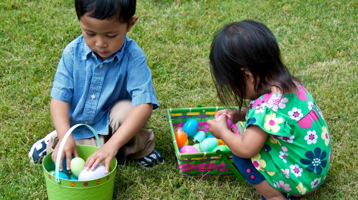 Two small kids brother and sister sitting in the grass and inspecting their Easter baskets full of plastic eggs