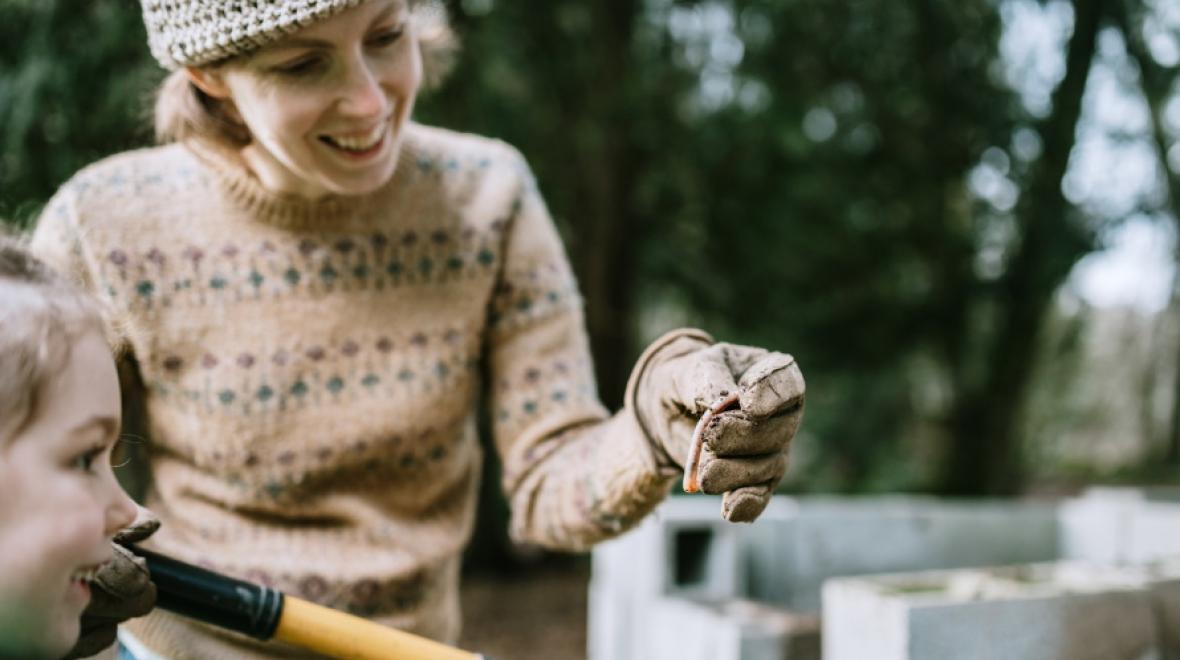 mother and daughter looking at a worm that the mom is holding in a gloved hand