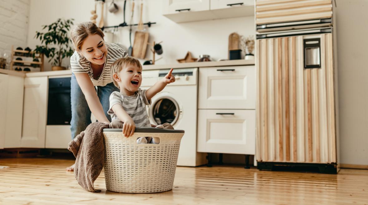 mom pushing her smiling son across the floor in a laundry basket