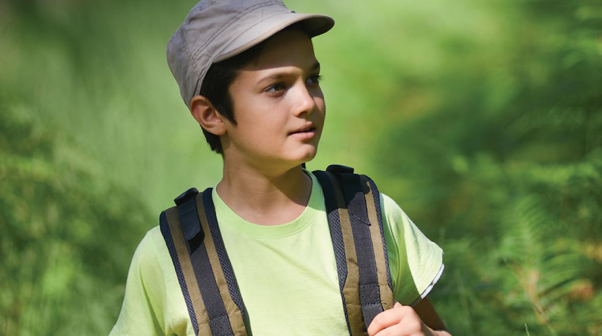 boy wearing a hat and backpack surrounded by green vegetation 