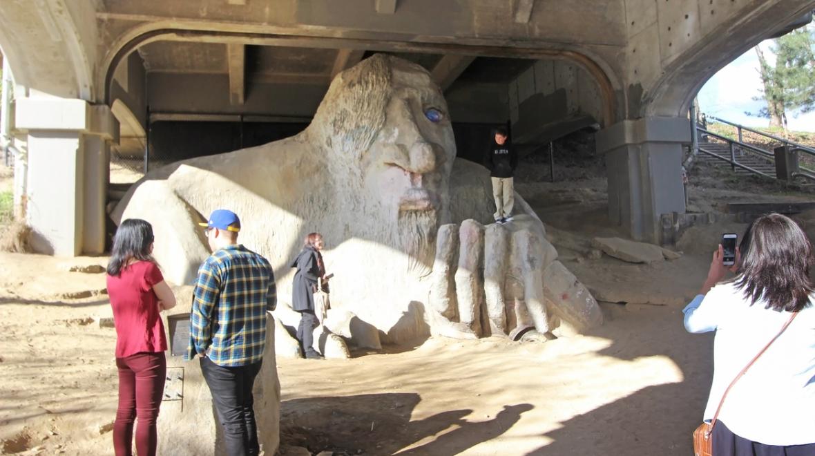Fremont troll statue sits under Seattle's Aurora Bridge in the Fremont neighborhood, boy posing for photo while people look on best instagram sights in seattle