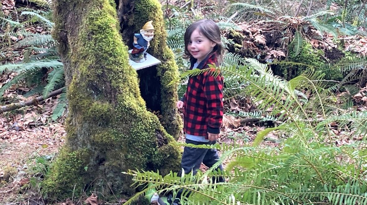 Kid in plaid jacket standing by gnome in tree along Maple Valley gnome trail fun for Seattle-area families