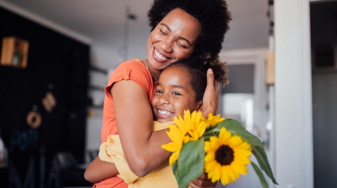 mother and daughter hugging with a vase of sunflowers on the kitchen table