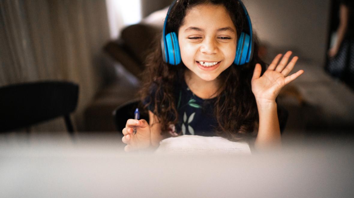 girl wearing headphones waving at her computer