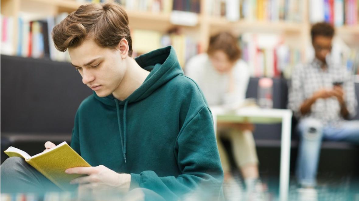 Student guy reading a book in a library 
