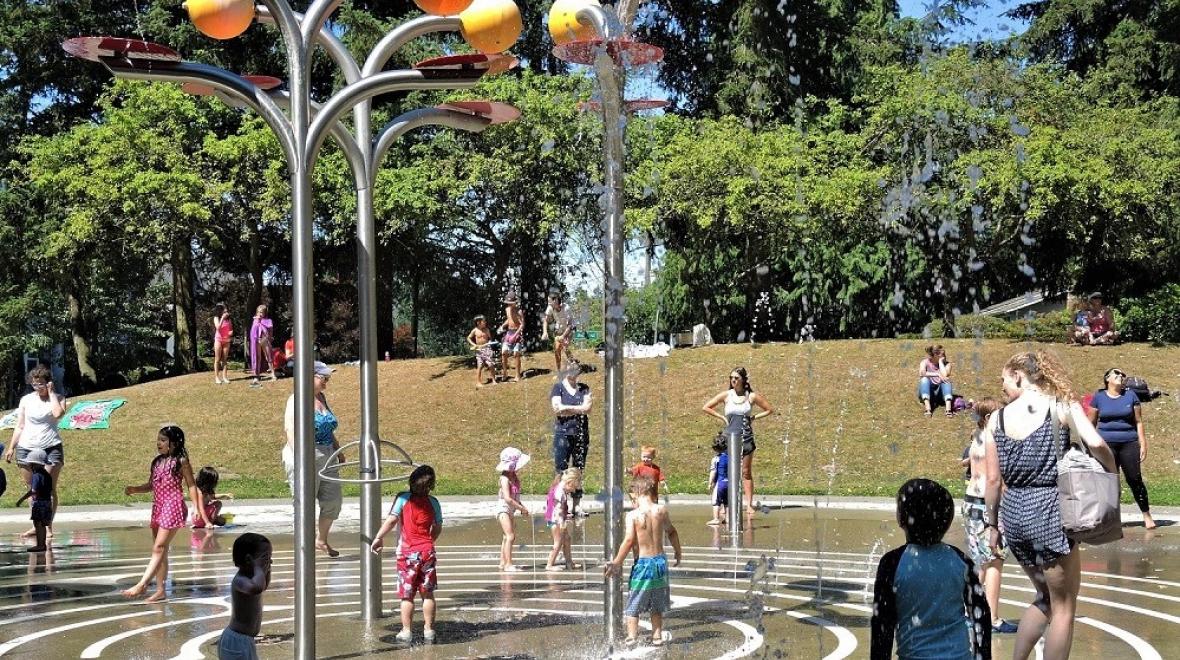 Young kids with parents watching play at Northacres Park in Seattle spray park on a warm summer day