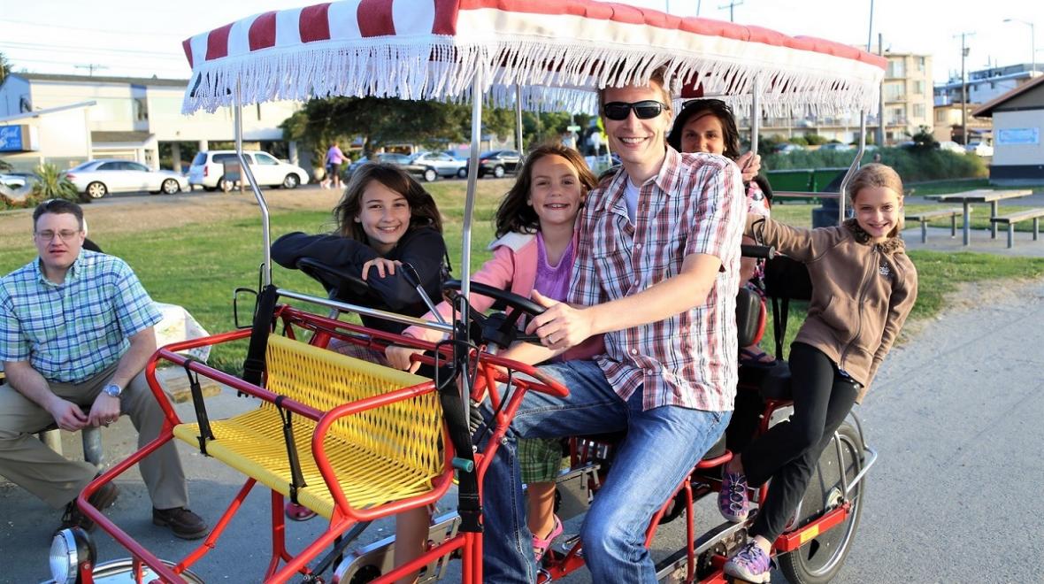 Family riding a surrey-style carriage bike along Alki Beach in Seattle best family activities to celebrate summer with kids