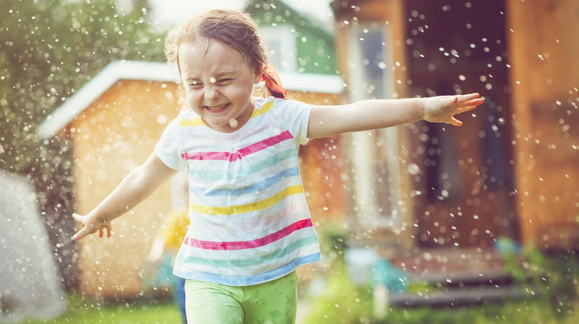 closeup of a girl running through a sprinkler with her arms out