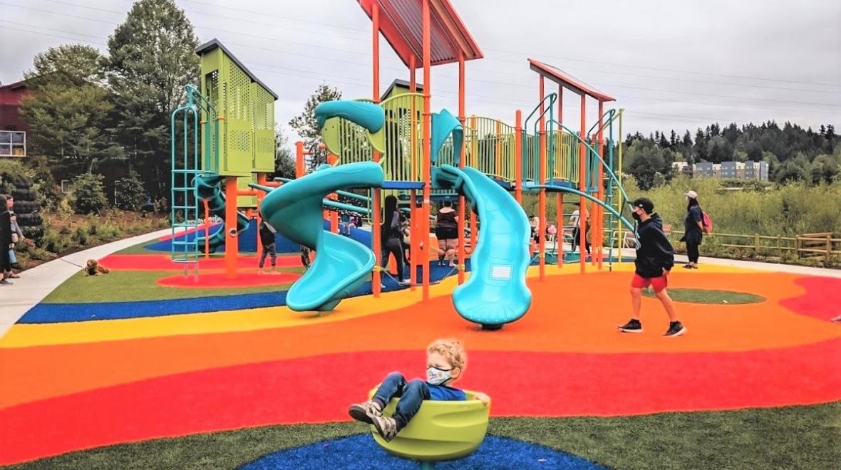 boy in a teacup play fixture with a colorful turf playground in the background at totem lake playground