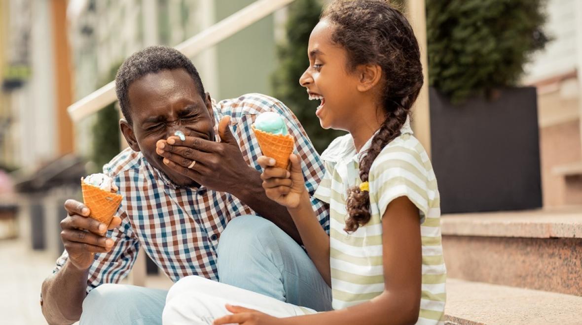 A dad and his young daughter laugh together while enjoying an ice cream cone