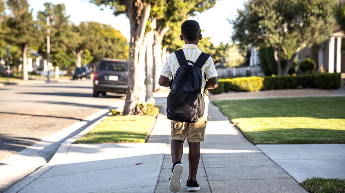boy wearing a backpack walking alone down a residential sidewalk