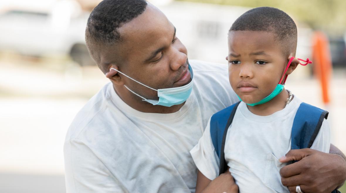 Father consoles anxious kindergartener while they wear masks as he's dropping him off for first day of school