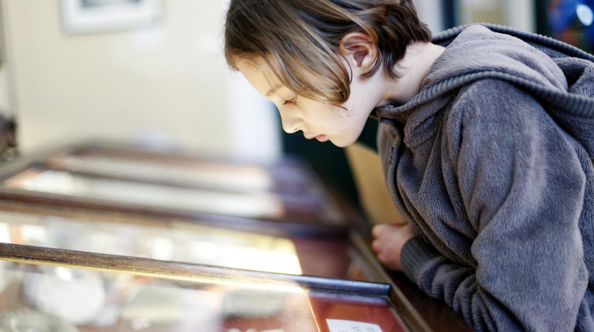 girl looking at a museum display with artifacts behind a glass panel