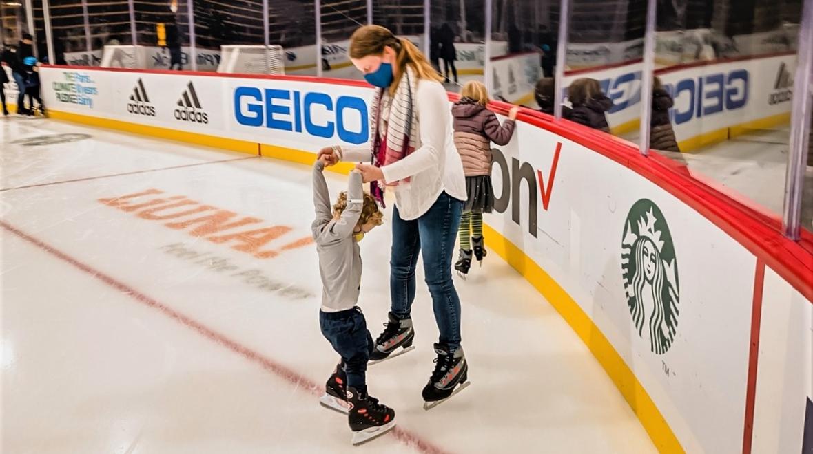 A mom and her two-year-old son hold hands ice skating at Seattle's new Kraken Community Iceplex new skating rink