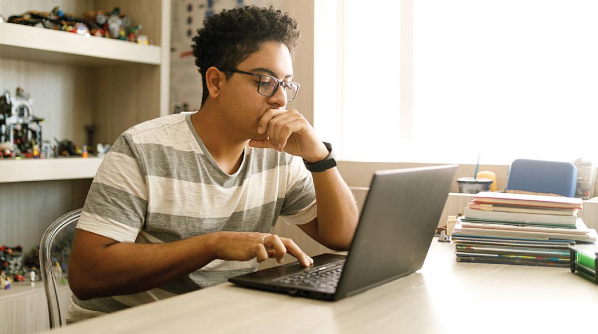 teenage boy with glasses working on a laptop