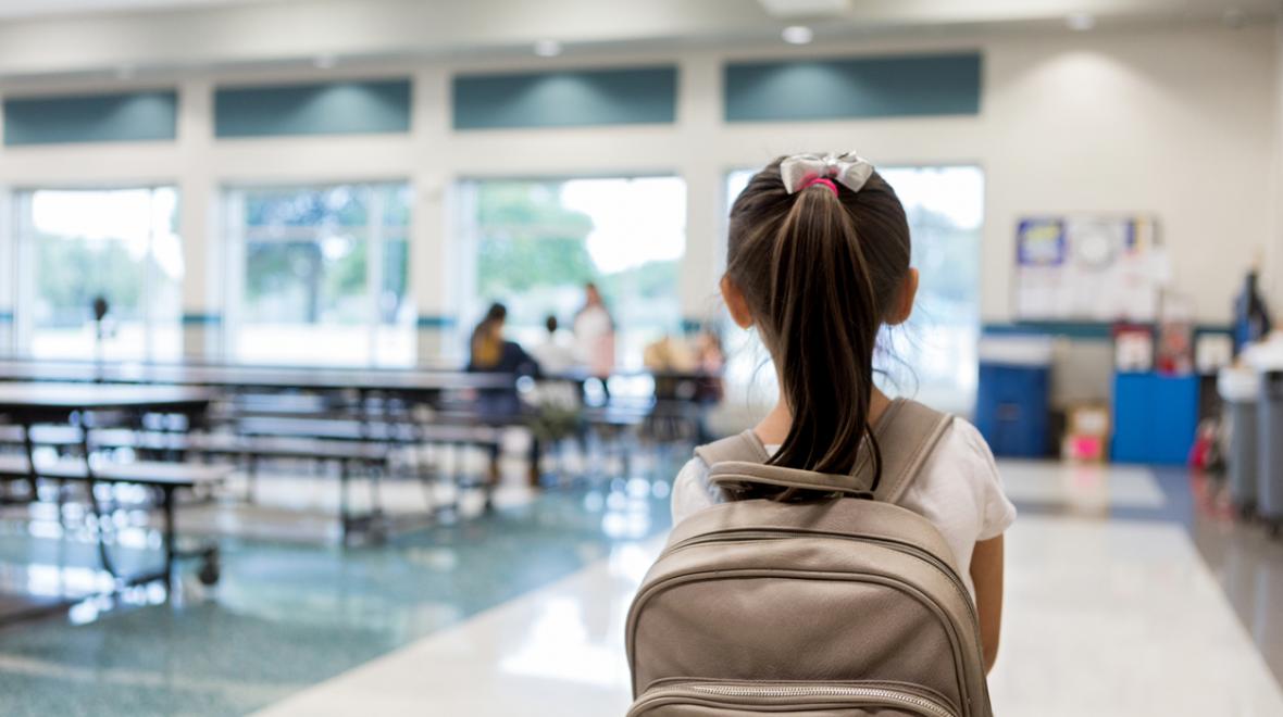 rear view of a girl with a backpack entering a relatively empty school cafeteria