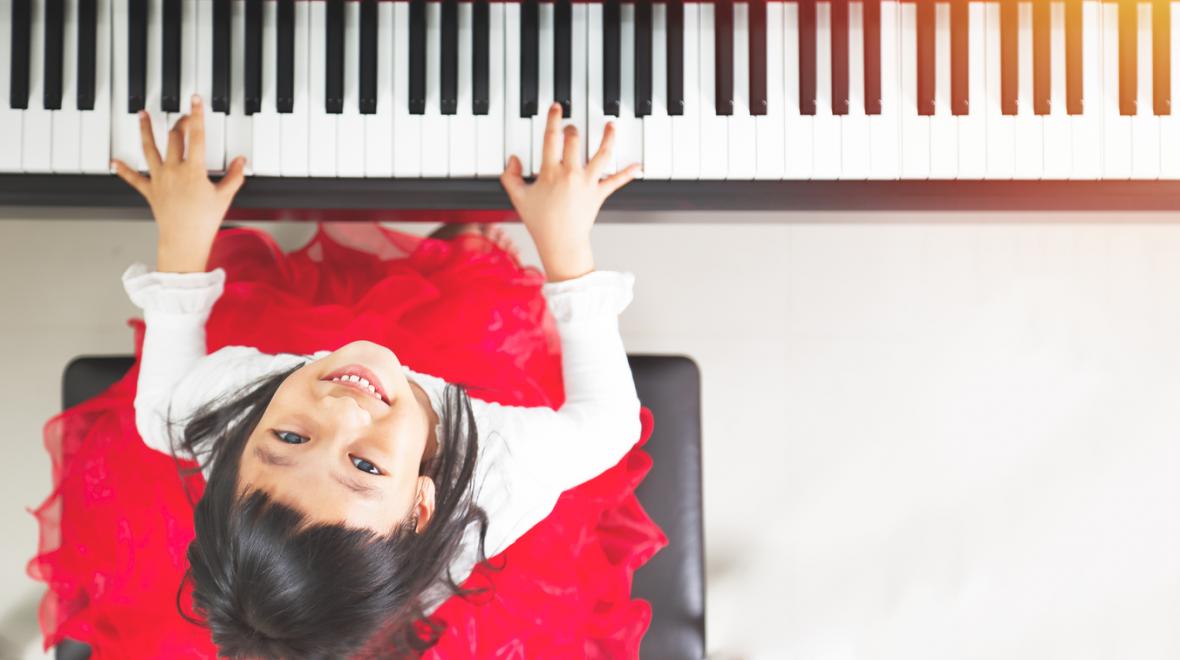 top-down photo of a girl in a red dress playing the piano while looking up at the camera
