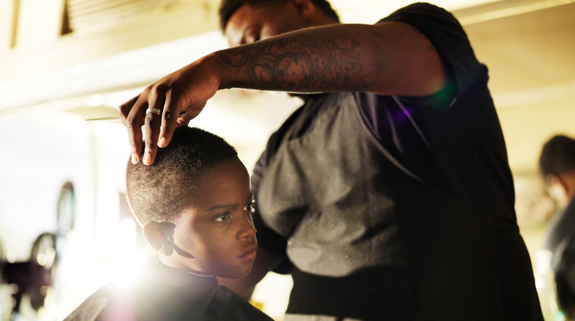 black barber with tattoos cutting the hair of a young black boy