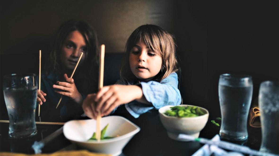 Two kids are eating in a restaurant with their family trying new foods using chopsticks best global dining destinations Seattle families