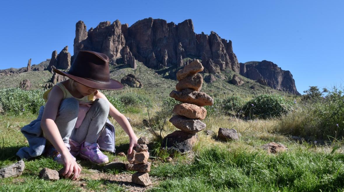 Young girl wearing hat is stacking rocks intently at Lost Dutchman State Park near Phoenix Arizona best sunny destinations one flight away from Seattle