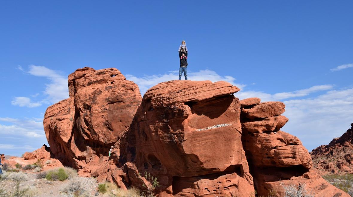 A dad with child on his shoulders poses on top of a rock formation at Valley of Fire near Las Vegas best sunny destinations one short flight from Seattle