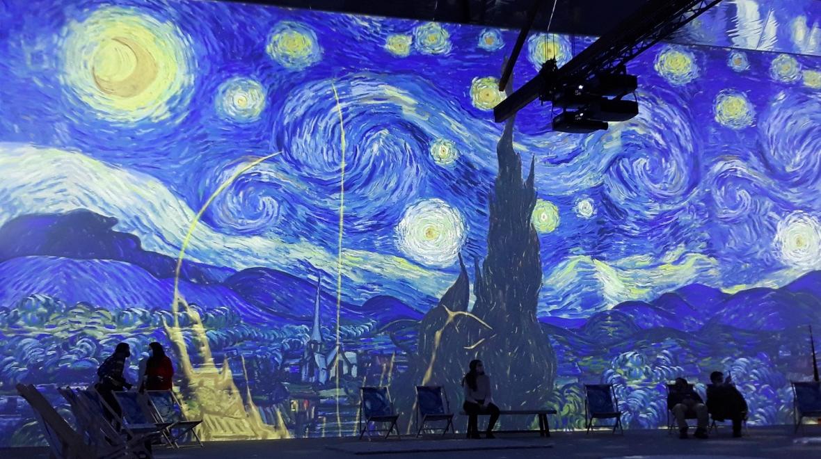 People look on as a digital projection of Van Gogh's Starry Night painting appears on the wall at Van Gogh: The Immersive Experience in Seattle