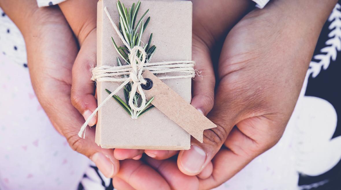 A parent holds her child's hands around a beautifully wrapped holiday present